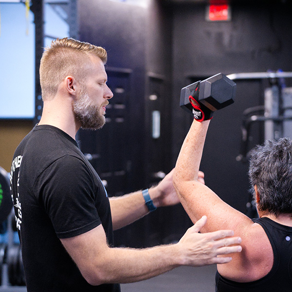 Coach Jesse adjusting a woman's form while she lifts a dumbbell
