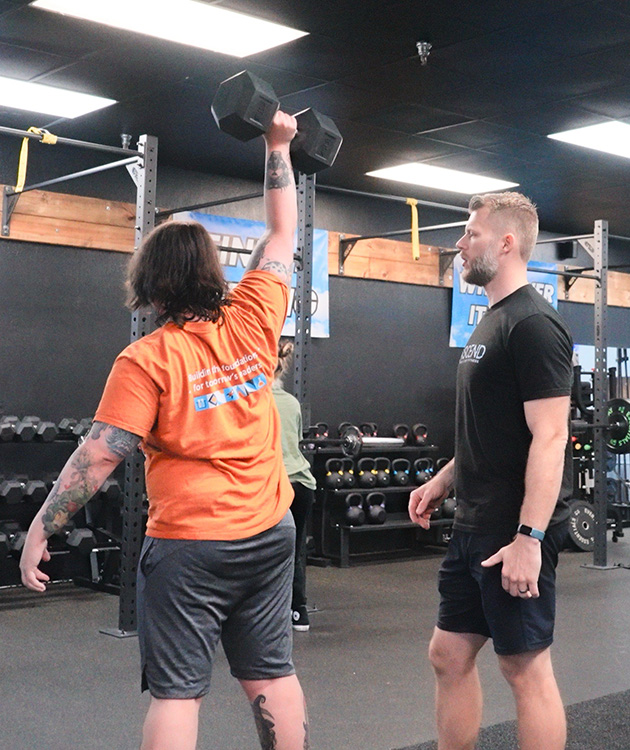 A man lifting a dumbbell in the air with his coach watching his form